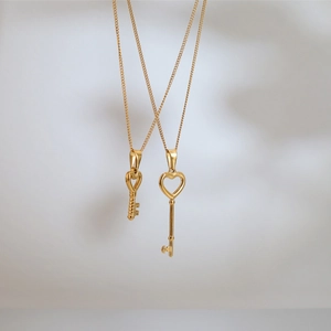 Detail view of two gold heart key pendants in titanium steel on minimalist background