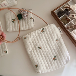 Detail of white quilted crossbody bag with orange floral embroidery and mushroom charm