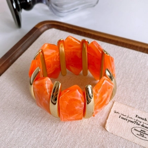 Detail of orange resin and gold metal segments on wide elastic hulu bracelet