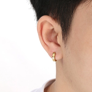 Macro shot of gold-plated hoop earring with engraved cross and small inlaid gemstone