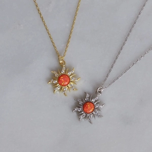 Gold and silver sun pendant necklaces with orange opal and zircon on marble background