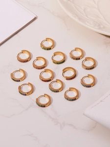 Macro shot of U-shaped gold earrings with colorful zircon stones on marble