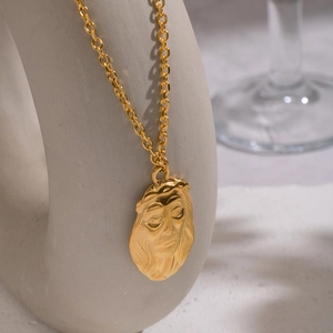 Détail d'un pendentif visage doré en relief sur une chaîne en acier inoxydable de luxe