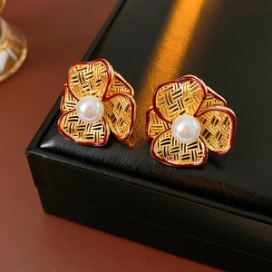 Close-up of gold flower earrings with red enamel edges and white pearl centers on leather