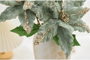 Gros plan d'une fleur de Noël artificielle vert sauge avec paillettes dorées et perles
