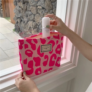 Detail of pink leopard print canvas tote bag being filled with cosmetics by model