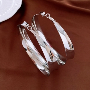 Détail de grandes boucles d'oreilles argentées géométriques sur fond de satin sombre