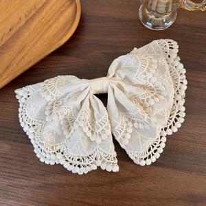 Elegant beige lace bow hair clip with hollow embroidery on dark wooden background