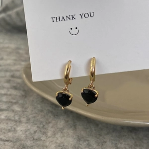 Detail of gold heart earrings with black zircon stones on a white Thank You card