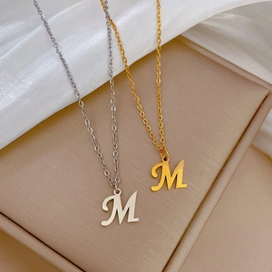 Detailed view of gold and silver M letter pendants on titanium steel necklaces