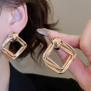 Close-up of geometric layered gold square earrings showing glossy finish and multi-layer design