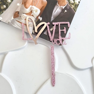 Dettaglio del cake topper LOVE you in acrilico rosa glitterato su una superficie bianca