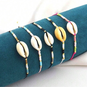 Five bohemian hand-woven shell bracelets with colorful beads on a blue display stand