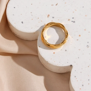 Close-up of golden wavy twisted ring on white cloud stand with beige silk backdrop