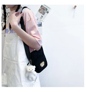 Detail of black corduroy crossbody bag featuring a bear badge and plush bear charm