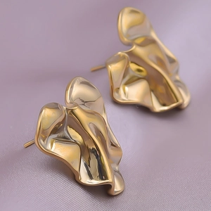 Close-up of golden irregular wrinkled heart earrings on purple textured background