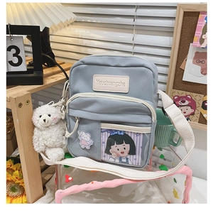 Détail du sac bandoulière en toile bleu clair avec breloque ours et broches