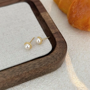 Elegant pearl stud earrings with gold rim on wooden tray with linen lining