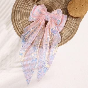 Pink sequin oversized bow hair clip with long ribbons on a woven mat with soft shadows
