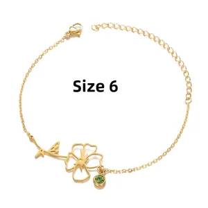 Detail of gold birthstone bracelet featuring a floral charm and green zircon gem