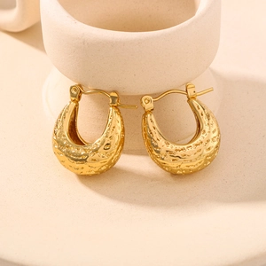 Golden U-shaped stainless steel earrings with textured hammered finish on ceramic tray