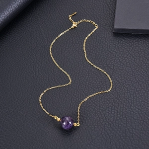 Minimalist gold necklace with a round purple crystal pendant on black leather background