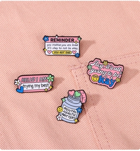 Close-up of four pink and purple enamel mental health awareness badges on denim fabric
