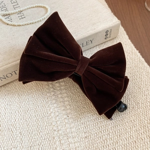 Detail of dark brown flocked bow hair clip on a vintage beige textured background