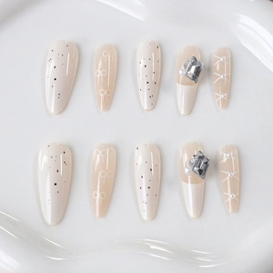 Detail of luxury almond fake nails with white bows, pearls, and crystals on cream base