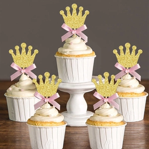 Detail of gold glitter crown cake toppers with pink bows on cream cupcakes