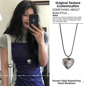 Macro detail of vintage heart pendant with intricate floral engravings on black cord