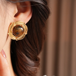 Macro shot of vintage gold earrings with brown tiger eye stone on a model's ear