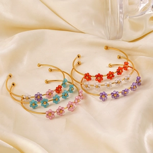 Elegant gold open cuff bracelets with colorful woven zircon flowers on silk background