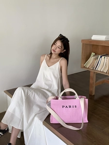 Pink woven straw tote bag with black PARIS embroidery shown in a lifestyle beach setting