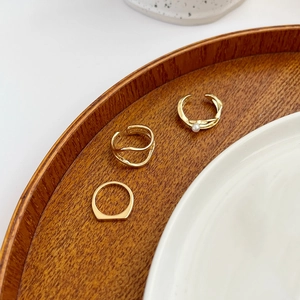 Detail of three gold geometric rings with a pearl on a textured wooden tray