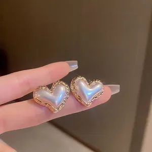 Close-up of heart-shaped earrings featuring white pearl inlay and golden wavy metal border