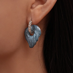 Close-up of beaded silver hoop earrings with dark marble resin leaf pendants on a model