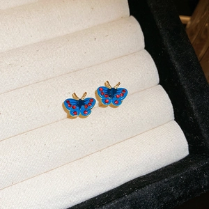 Puces d'oreilles papillon vintage en émail bleu et strass rouges sur boîte à bijoux