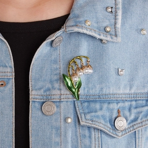 Close-up of a lily of the valley brooch with white pearls on a blue denim jacket