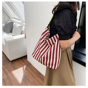 Detail of red and white striped tote bag with contrasting green pleated handles shown in use