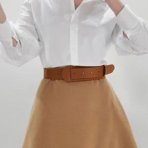 Close-up of a stylish brown leather waist belt styled with a white shirt and khaki skirt