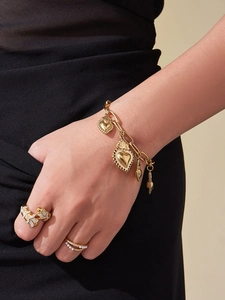 Détail d'un bracelet doré à breloques cœur avec bagues perle et feuille sur la main