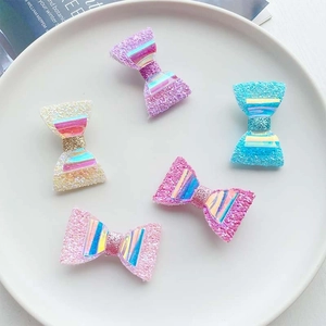 Flat lay of 5 glitter bow hair clips in pastel colors on a white ceramic plate