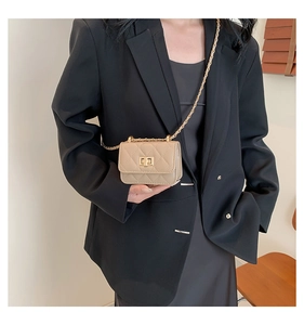 Close-up of a mini quilted beige crossbody bag with a gold chain strap on a model