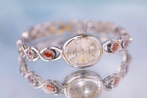 Detailed close-up of oval quartz watch with silver strap and colorful inlaid gemstones