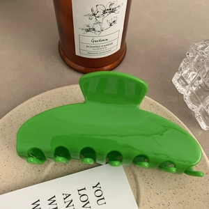 Detail view of a large green acetate hair claw clip on a textured decorative plate