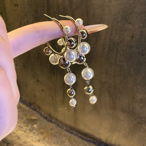 Elegant gold C-shape drop earrings with pearls and tassel, held for a detailed view