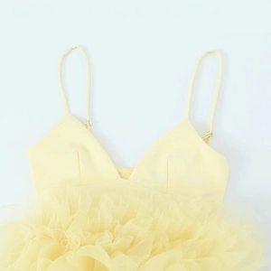 Gele camisole top met V-hals en gelaagde tule zoom plat gelegd op witte achtergrond