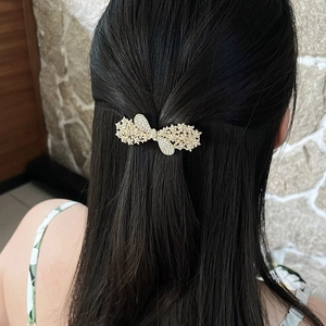 Elegant gold bow hair clip with pearls and rhinestones shown on a model's hair