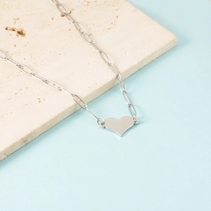 Detail of silver heart pendant necklace with paperclip chain on stone texture background